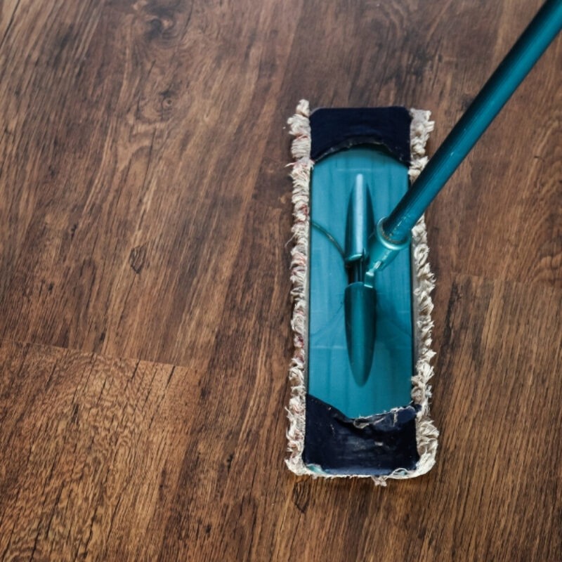An image looking down on a dark brown hardwood floor with a blue dust mop in the center right of the image