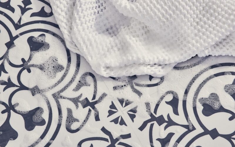 A close up image of decorative navy and white flooring with soap suds and a white wash cloth.