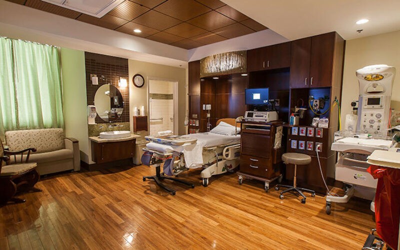 A room scene of a labor delivery room with warm wood flooring and neutral colored finishes